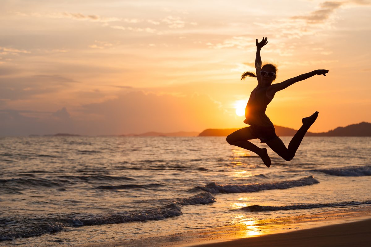 Happy girl jumping on the beach at sunset time enjoying life.