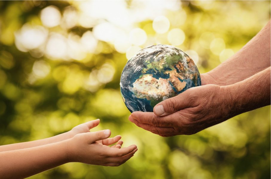 Close up of senior hands giving small planet earth to a child over defocused green background as a sign of sustainability.